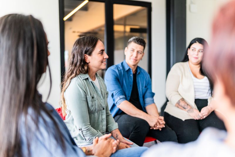 Adults sit in a circle during a group therapy session as one participant shares and others listen
